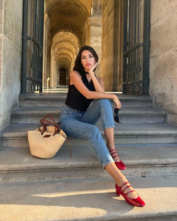 Modelo usando calça jeans e camisa preta com sapato Mary Jane vermelho.