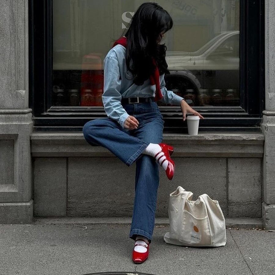 Modelo com look total jeans com sapato vermelho e meia.