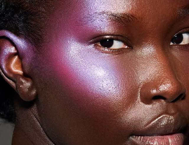 Modelo negra em close-up usando blush lilás furta-cor com acabamento glow na bochecha.