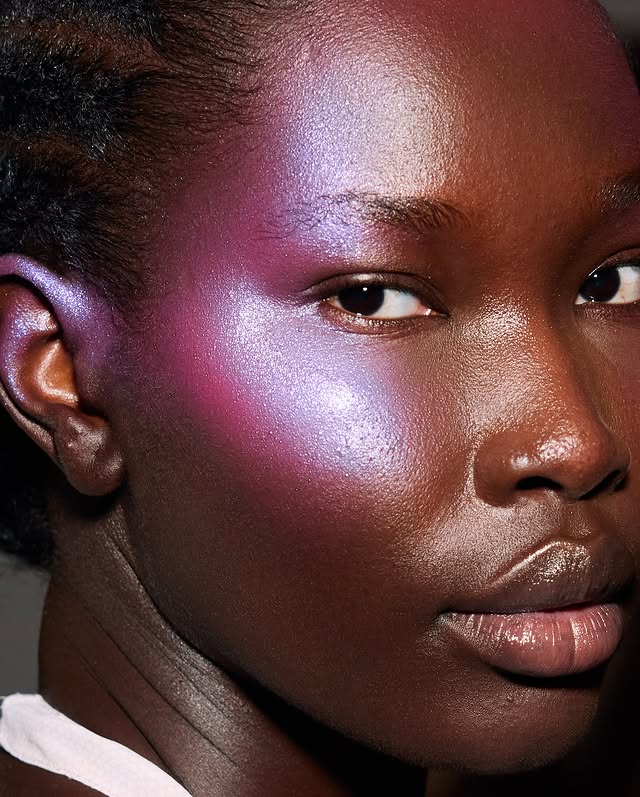 Modelo negra em close-up usando blush lilás furta-cor com acabamento glow na bochecha.